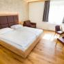 Modernly furnished hotel room with double bed, desk, chairs and an armchair.