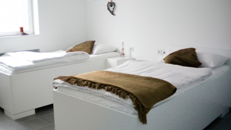 UHL workers' quarter, © Arbeiterquartier UHL Two white beds in a bright room with brown blankets and pillows.