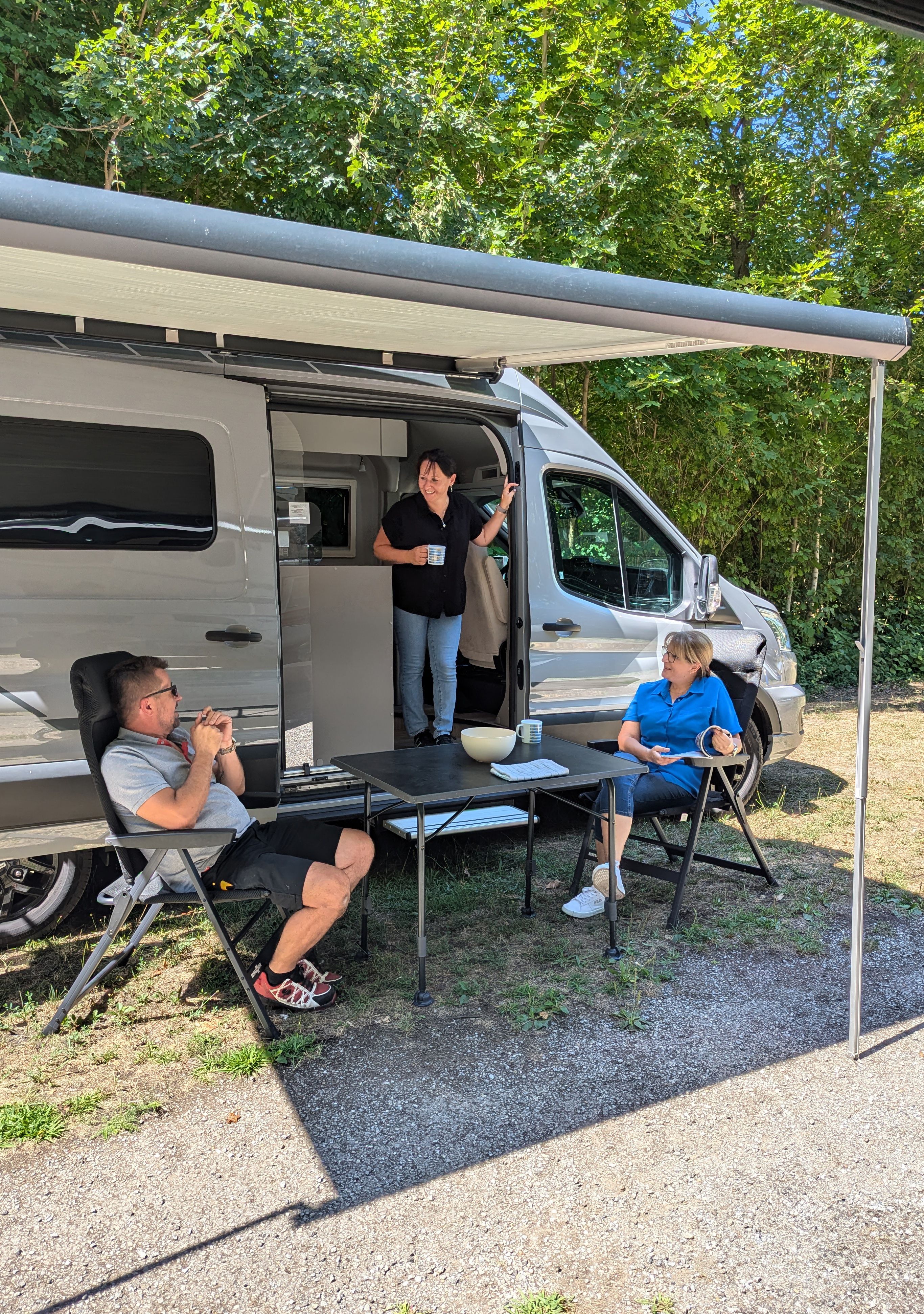 Three people relaxing in front of a mobile home in the open air.