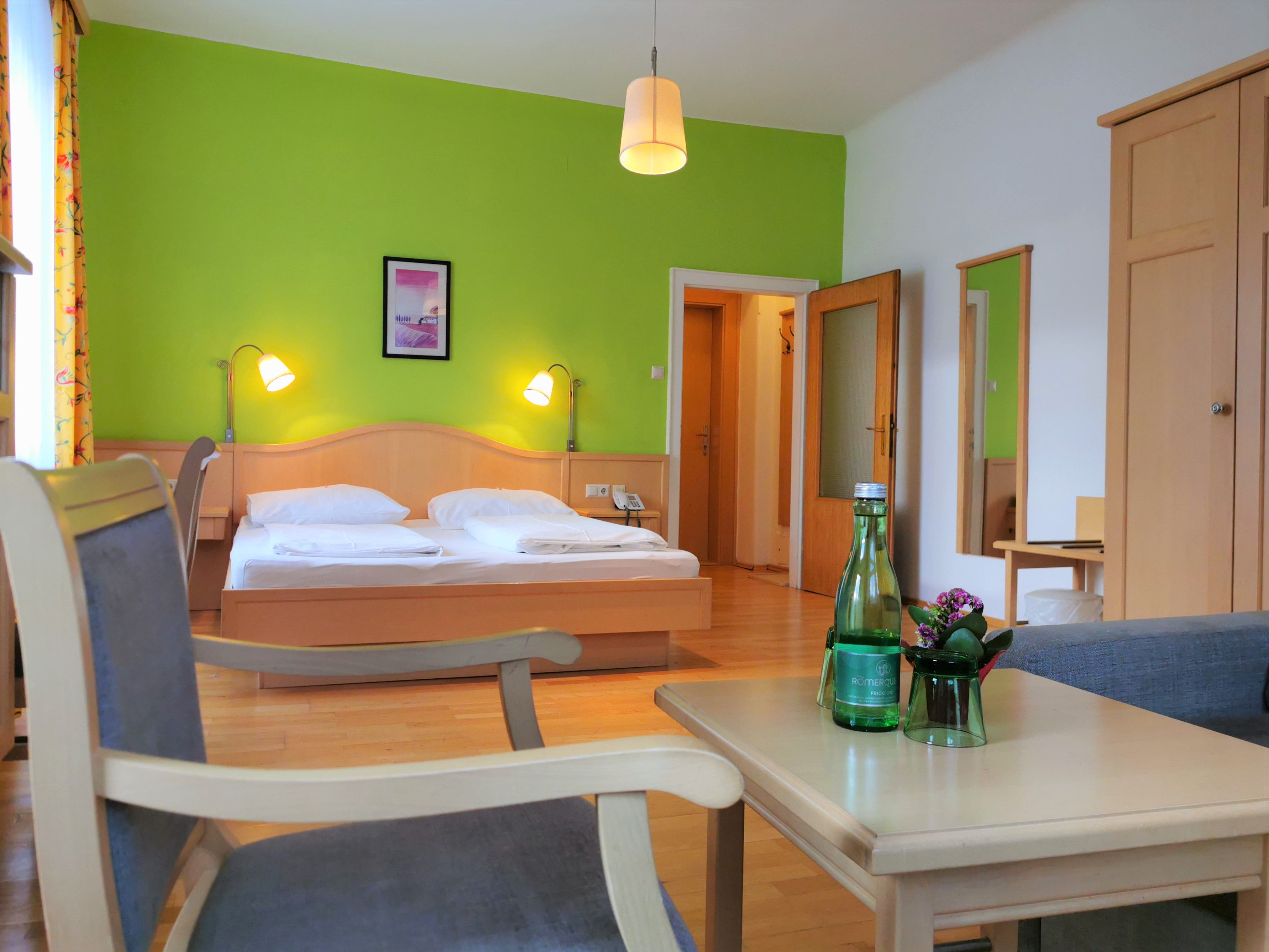 A cozy double room with green-painted wall, double bed, table, chairs and water bottle.