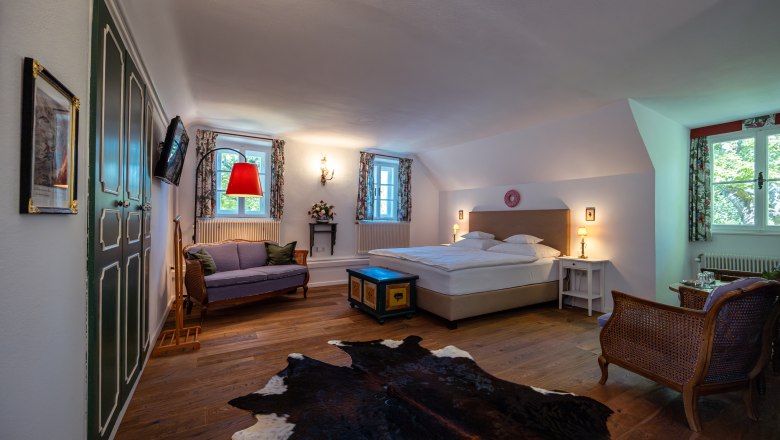 Cozy bedroom with double bed, sofa, wooden floor and cowhide carpet.