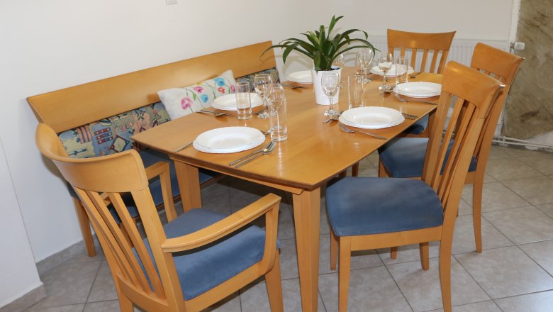 Dining area with wooden table, six covered seats and blue chairs.