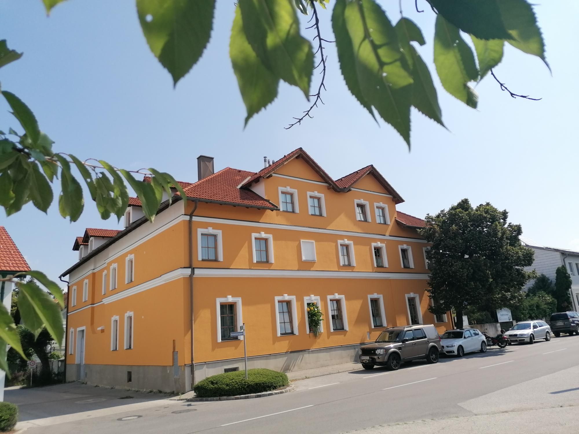 Yellow building with red roofs, surrounded by trees and parked cars.