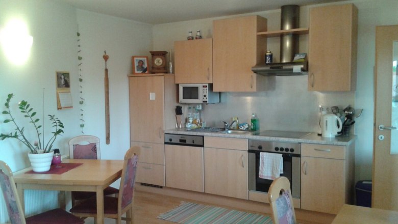 A cozy kitchen with wooden furniture, dining table, chairs, sink, stove and microwave. There are pictures and a calendar on the wall.