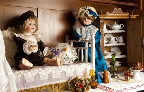 Two antique dolls in a nostalgic room with crockery and decorations.