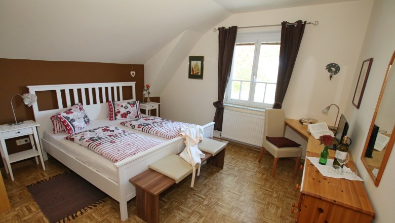 Cozy guest room with double bed, sofa, table and chair. Brown accent wall and dark curtains.