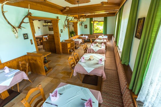 Cozy restaurant with wooden furniture and tablecloths, decorated with antlers on the walls.
