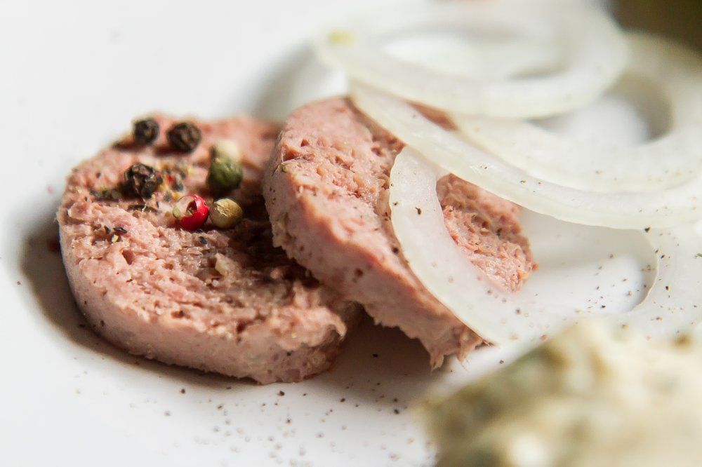 Close-up of slices of sausage with peppercorns and onion rings on a plate.