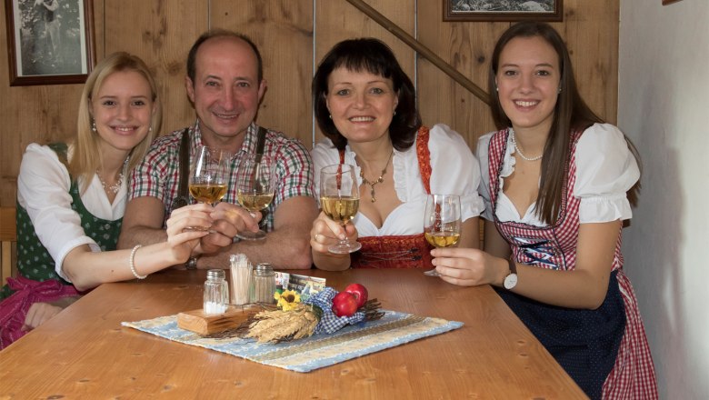 A family in traditional dress clinks glasses of wine at a wooden table.