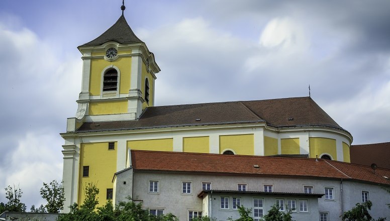 Yellow church with tower and red roofs against a cloudy sky.