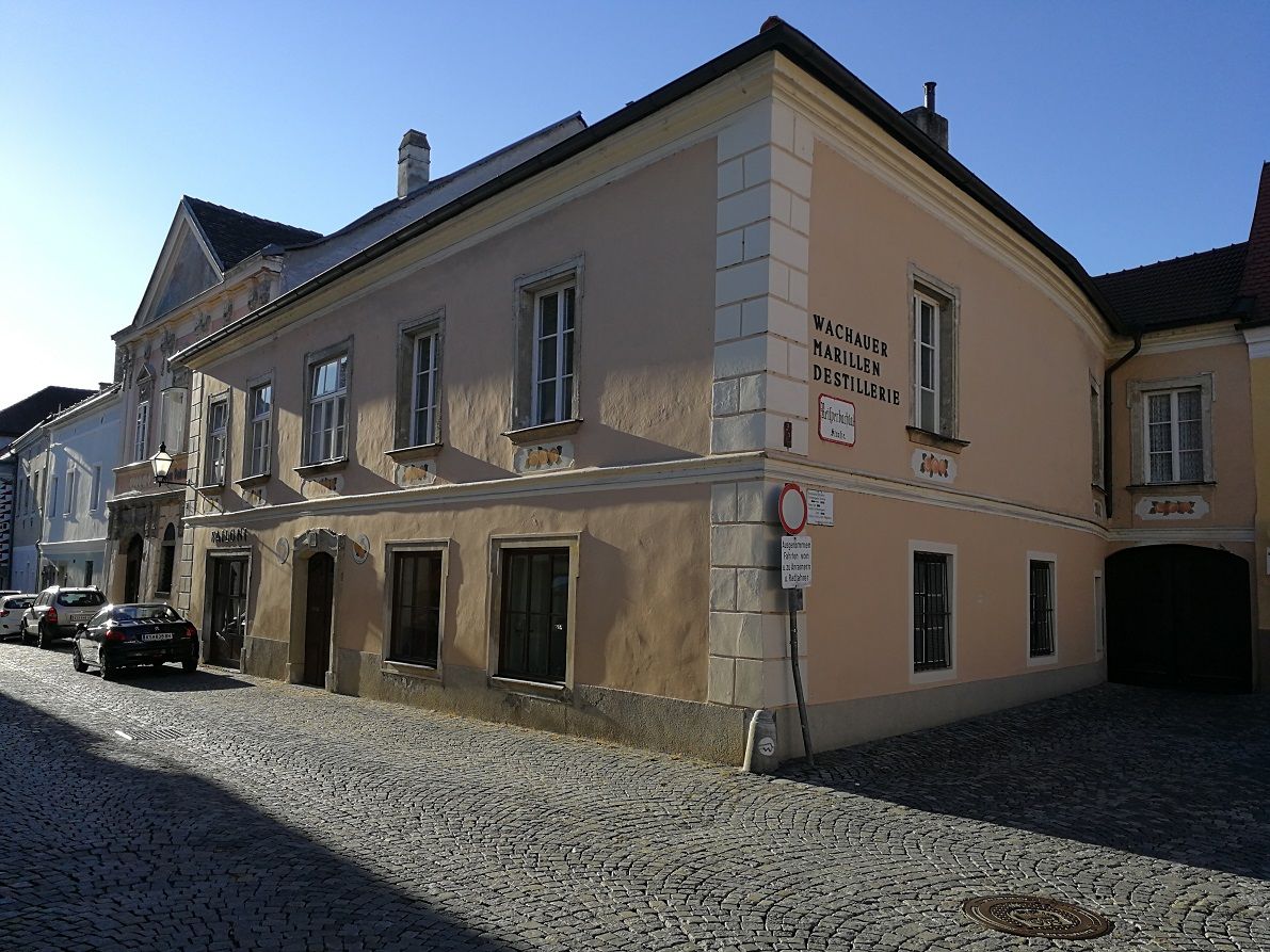 Historic building with the inscription 'Wachauer Marillen Destillerie' in a cobbled street.