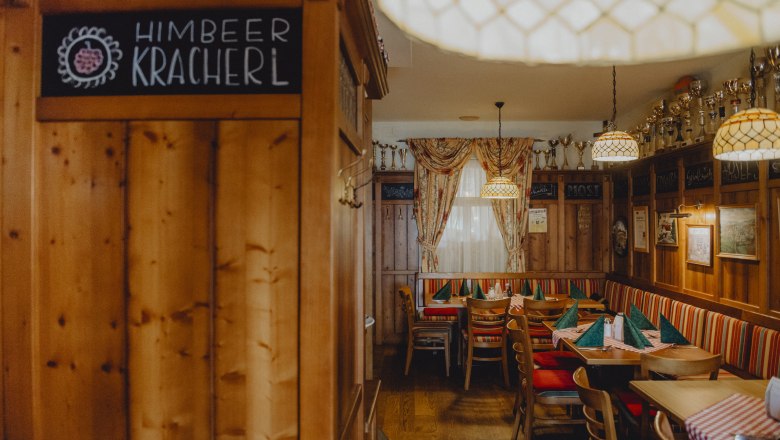 Cozy farmhouse parlor with wooden furniture, checkered tablecloths and goblets on a shelf.