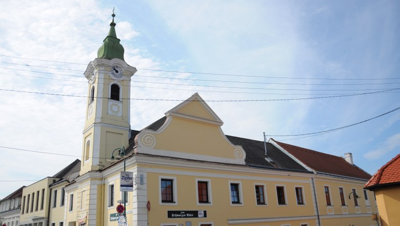 Yellow building with tower and clock, Gasthaus zum schwarzen Adler, blue sky.