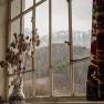 View from a window with mountain landscape in the background, vase with dried flowers in the foreground.