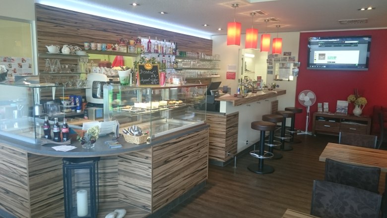 Interior view of a café with counter, bar stools and red wall.