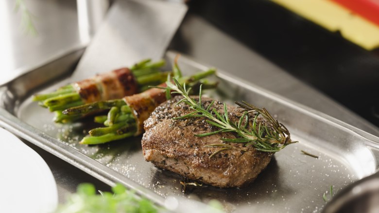 A steak with rosemary and beans wrapped in bacon on a metal tray.
