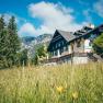 A traditional building called Knappenhof in a green meadow against a mountain backdrop.