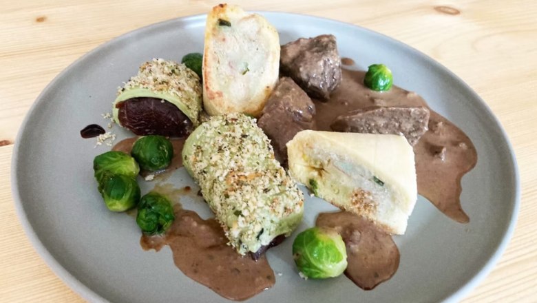 A plate of meat, Brussels sprouts and stuffed pastry rolls on a brown sauce.