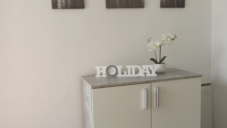 A white cupboard with decoration and three cityscapes on the wall.