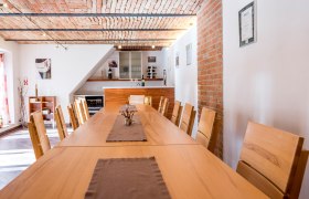 Tasting room with long wooden table and chairs, brick ceiling and wine rack.