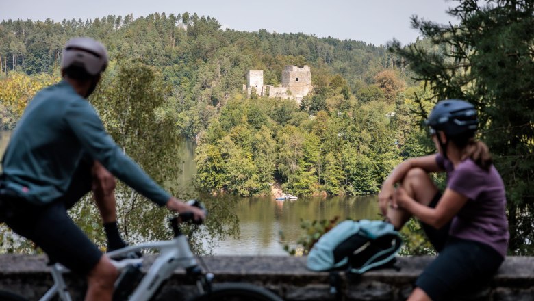 Two cyclists look at the Dobra ruins across a lake.