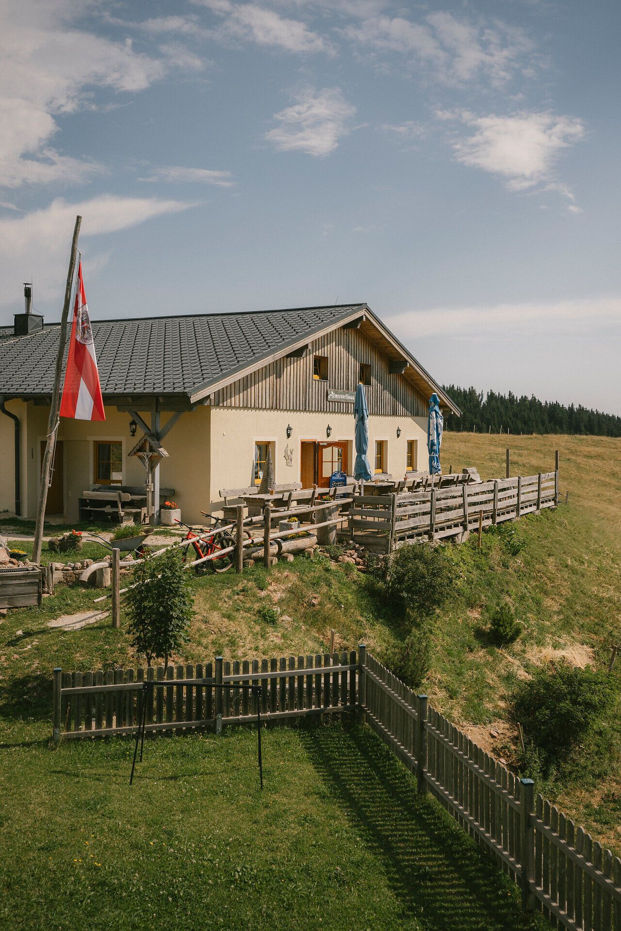 Exterior view of the Almreserlhaus on the Schneeberg, featuring a terrace and a flagpole