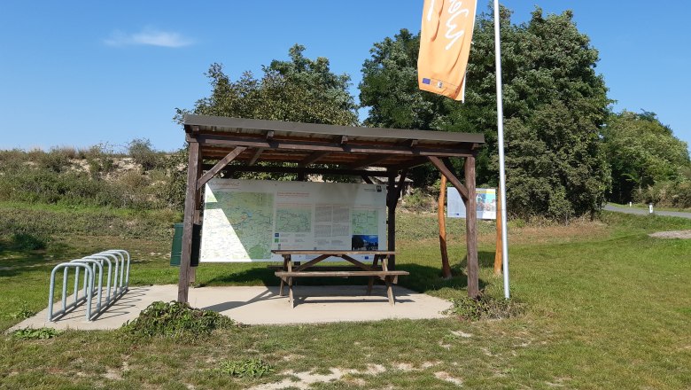 Rest station with covered table, bicycle stand and information boards in a green setting.