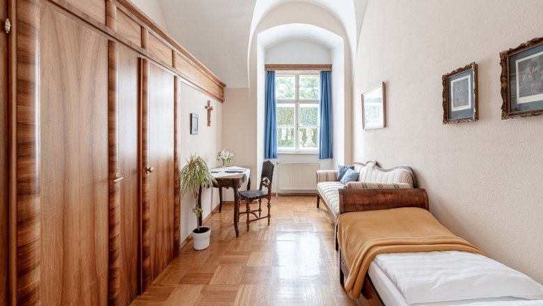 A traditionally furnished double room with two single beds, wooden furniture and a window with blue curtains.