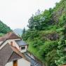 View from a terrace onto a house roof, surrounded by green trees and rocks.