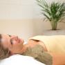 Woman relaxing with a sulphur mud pack on her shoulder, wrapped in a blanket, in the wellness area with a plant in the background.