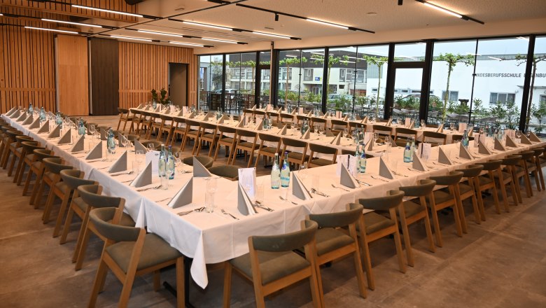 A large, modern seminar room with U-shaped tables, wooden chairs and large windows.