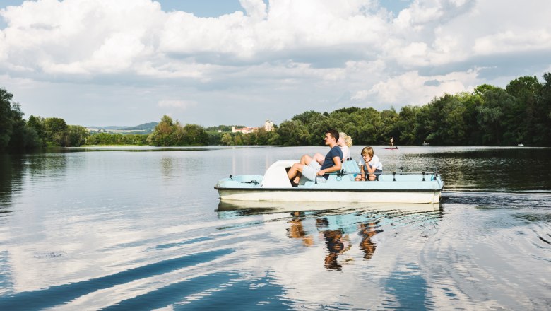 Family on a pedal boat on a lake with a cloudy sky.