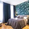 Modern double room with gray bed, tropical wallpaper and dark curtains.
