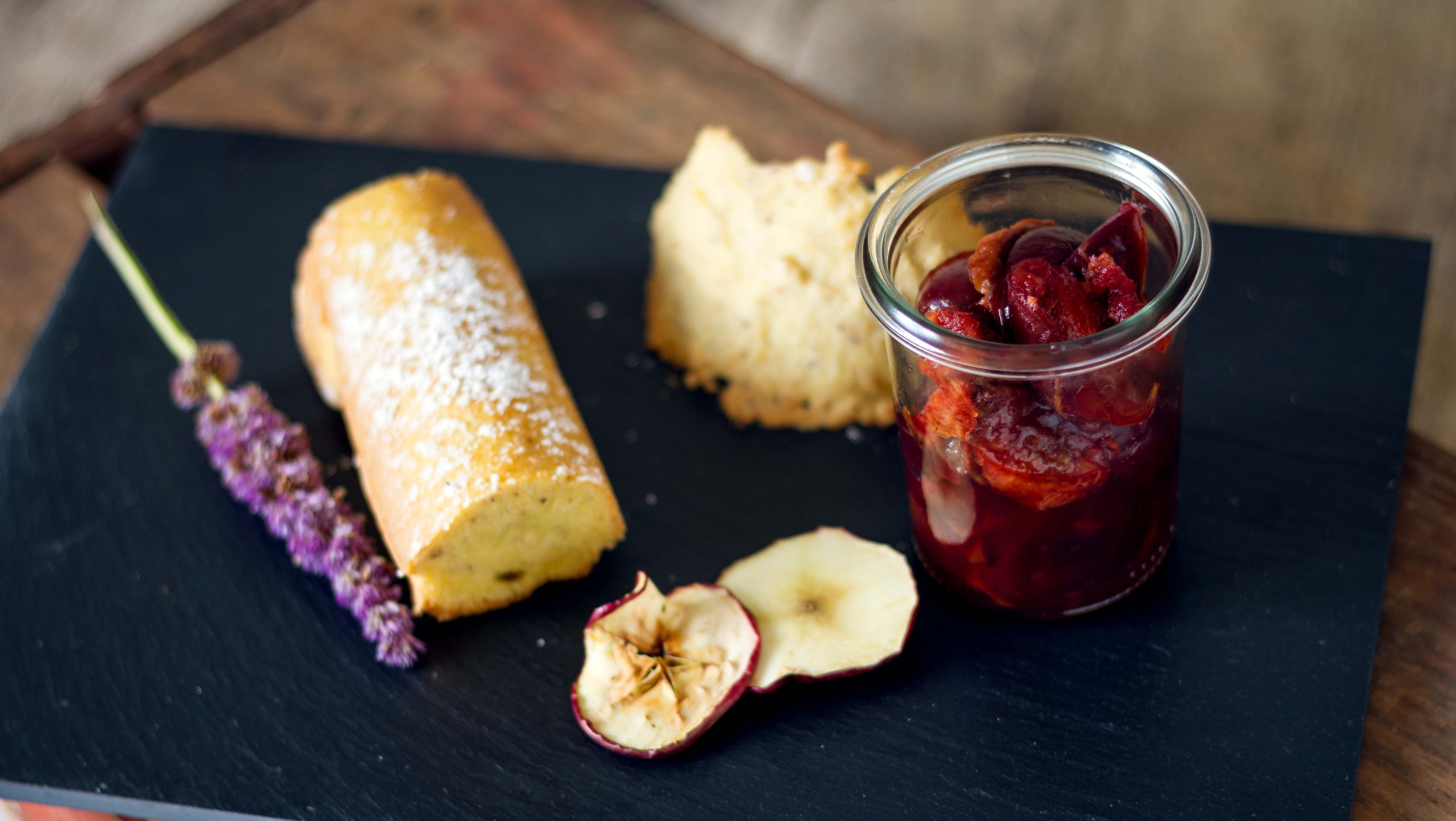 A rectangular plate with dried apple slices, fruit compote in a glass, ice cream, cake and lavender.