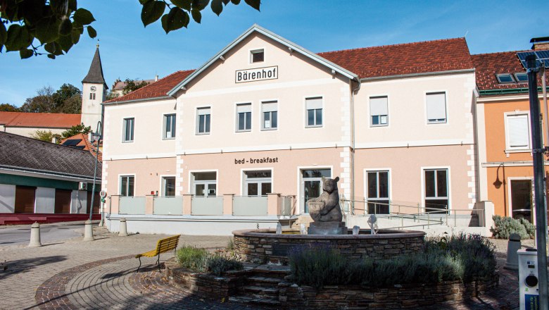 A building with the inscription 'B&auml;renhof' and 'bed - breakfast' in a sunny setting with a fountain in the foreground.