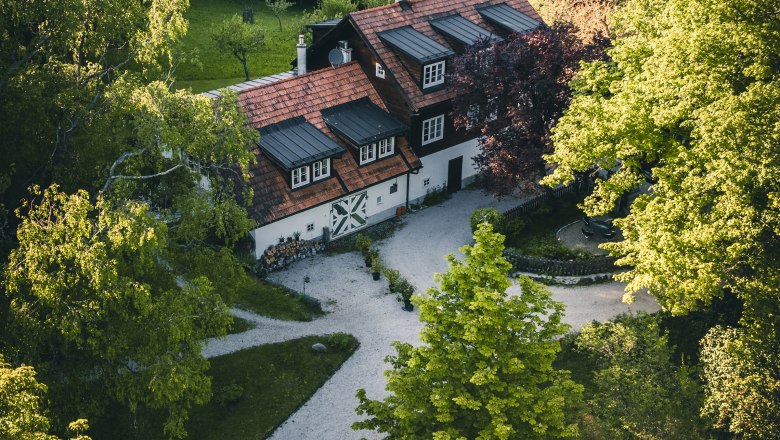 Aerial view of a traditional house in the countryside, surrounded by trees and a well-tended garden.
