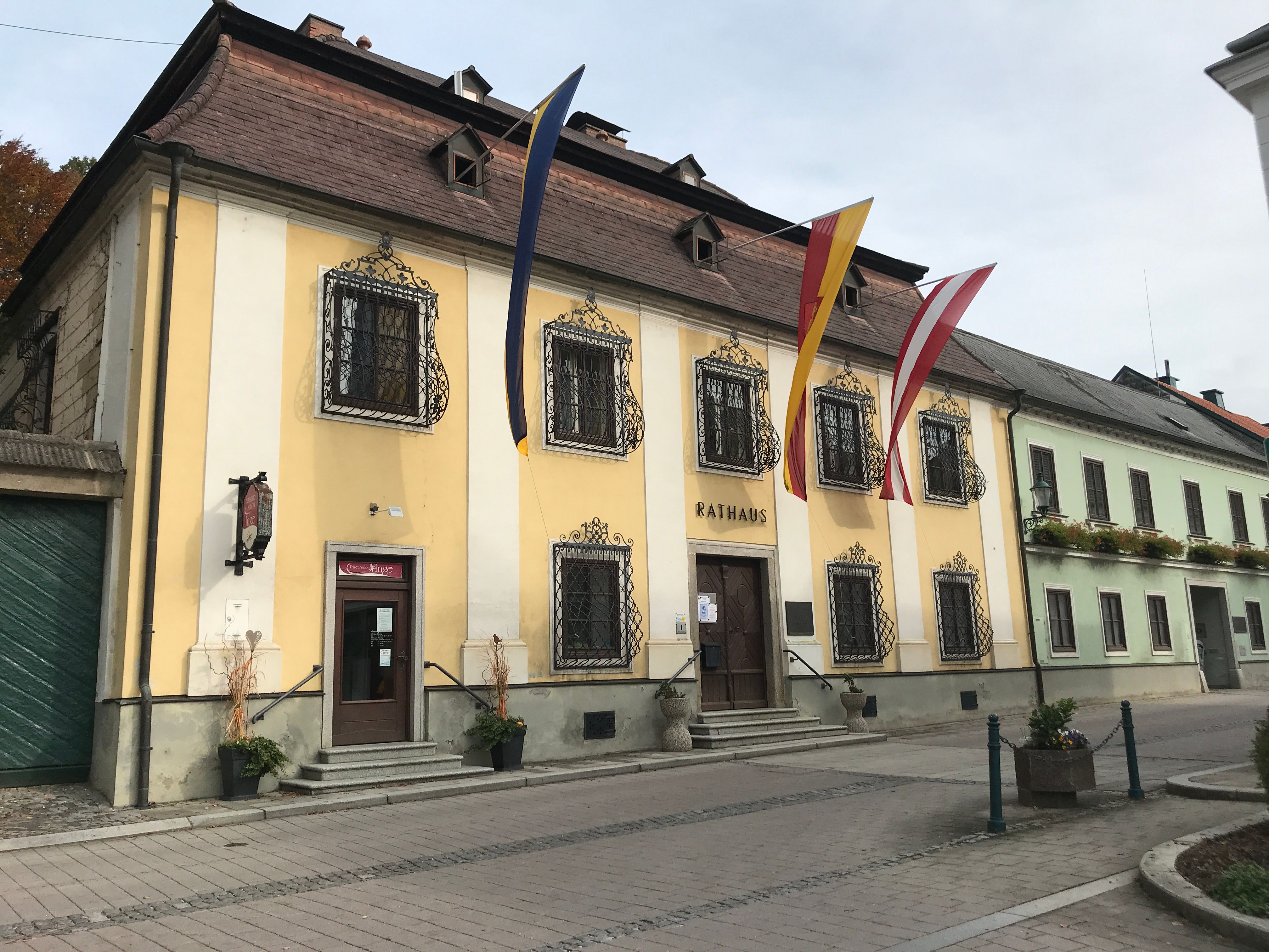 The Persenbeug town hall with its yellow façade and decorative window grilles, decorated with flags.