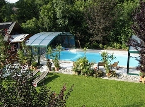 A covered outdoor pool with sun loungers and plants, surrounded by greenery.