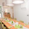 A bright dining room with a long wooden table, green chairs and decorations. 'AUFESSEN' is written on the wall.