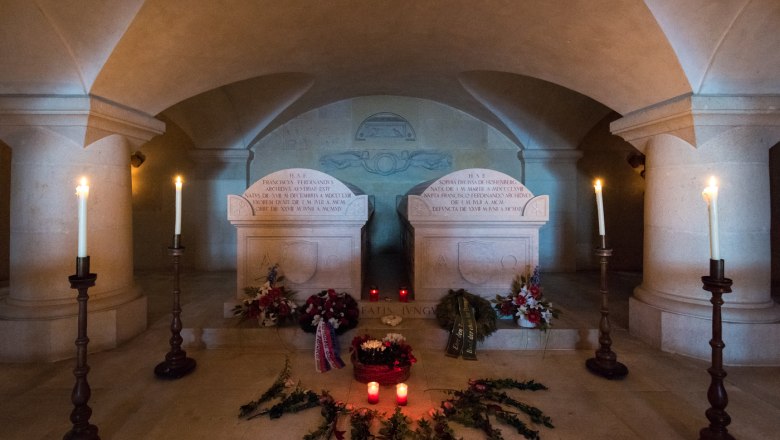 Interior view of a family tomb with two gravestones, candles and flowers.