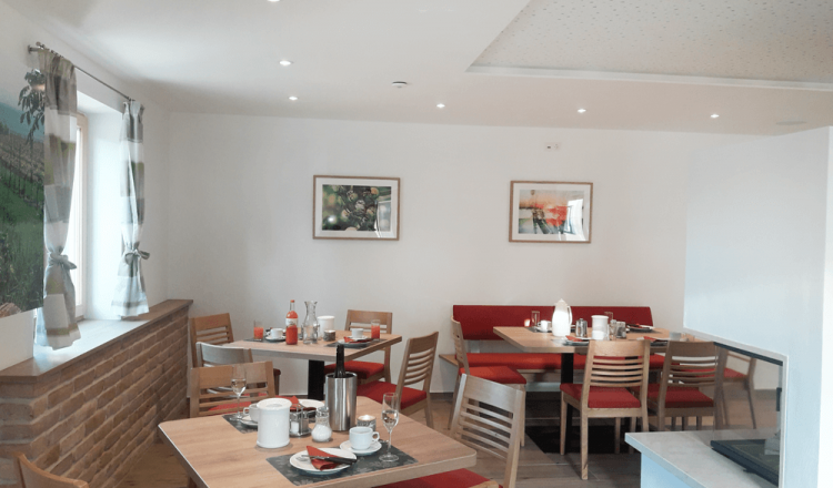 A cozy breakfast room with wooden tables, red upholstered benches and decorative pictures on the wall.