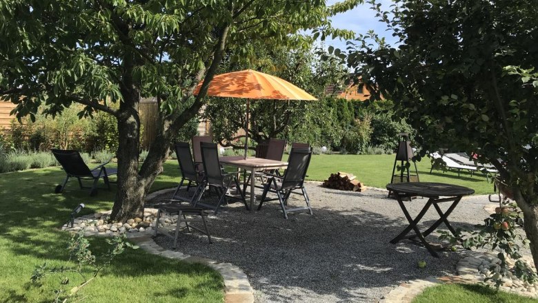 Garden with seating area under trees, table and chairs, orange parasol.