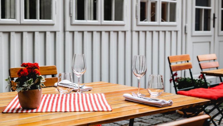 Wooden table set outside with flowers and glasses.