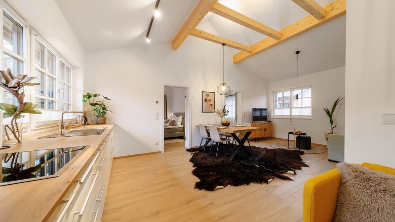 Apartment Mandelstein, © Göllitzhof Modern living room with wooden beams, dining table, yellow armchair and open kitchen.