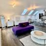 Modern loft with purple sofa, dining table and kitchen under skylights.