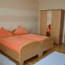 A cozy bedroom with two single beds, orange bed linen, a closet and bedside tables.