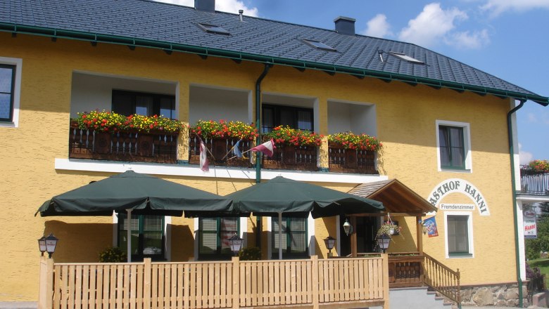 Gasthof Hanni KG, © Gasthof Hanni KG Yellow building with balcony, flowers and terrace with parasols.