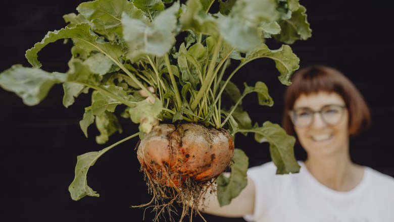 Woman holding a large turnip with leaves.