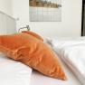 A bed with orange pillows and white bed linen in a guest room. A picture with hooks on tiles hangs on the wall.
