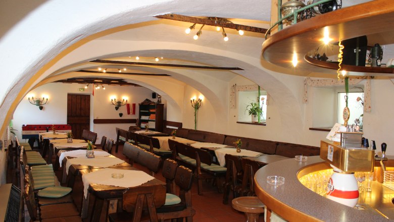 Interior view of a rustic bar with wooden tables and chairs, vaulted ceiling and counter.